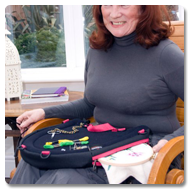 Bernie sits in a high-back chair, using the Trabasacking Curve Connect pink trim to aid crafting with thread