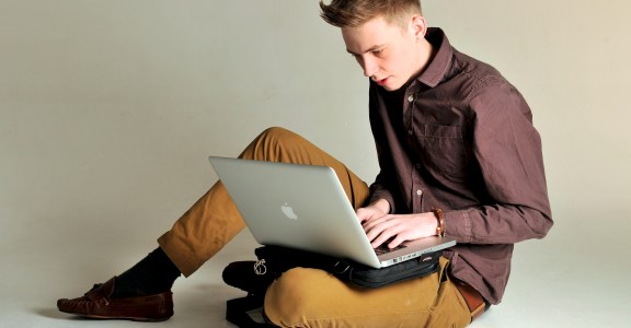 Young man sitting upon the floor using the Trabasack Mini upon his lap for his laptop