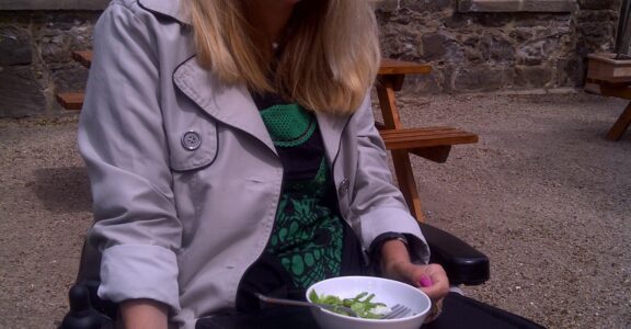 Image of a lady sat outside a pub, using the Trabasack as a wheelchair tray for dining-out