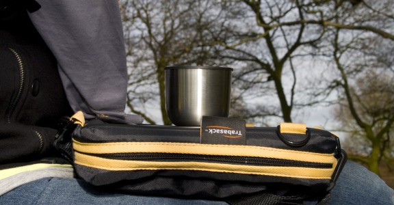Photo of Trabasack Mini on someone's lap with a cup on top, behind in the background is a forrest of trees