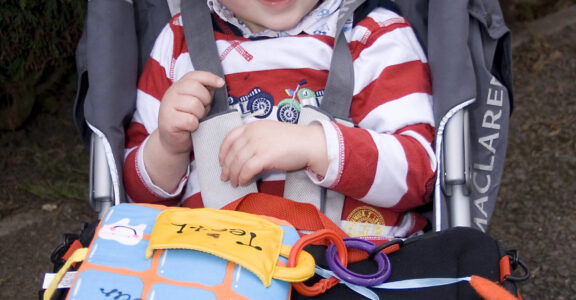 Young boy smiles to the camera whilst sitting in his buggy, with a Trabasack Curve Connect play tray on his lap