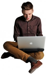 Young man sat cross-legged on the floor, using a laptop computer on top of a Trabasack lapdesk