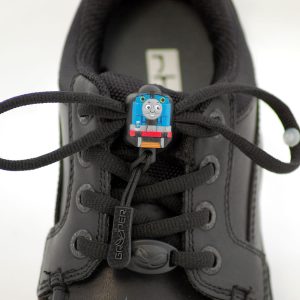 Photograph of a smart, black shoe with black Greeper laces which feature a small Thomas the Tank Engine motif in the centre
