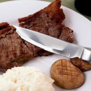 Photograph shows a plate of food with potatoes and steak, with the Knork Steak Knife cutting through the steak