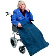 Image is a photograph of a middle-aged lady with bobbed blonde hair, sat in a wheelchair with a navy blue wheelchair leg protector