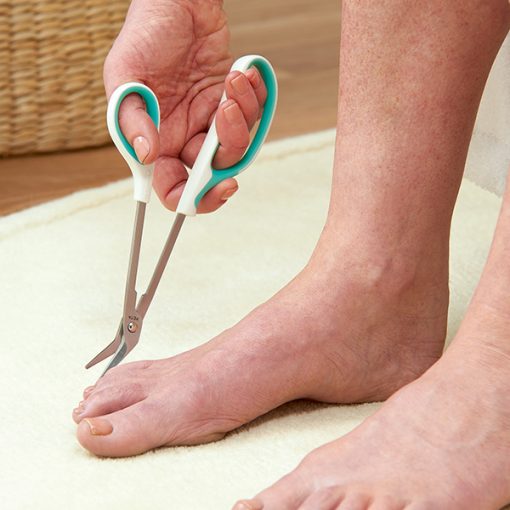 Image is a photograph of a person's feet on a mat, using the easi-grip long reach nail cutters to trim their toe nails
