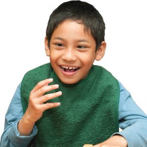 Image shows a photograph of a young boy, smiling with his hand raised, wearing a Racing Green coloured cotton apron