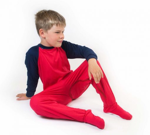 Image shows a photograph of a boy with light brown hair, sat casually on the floor wearing a Seenin jersey sleepsuit in navy blue and red