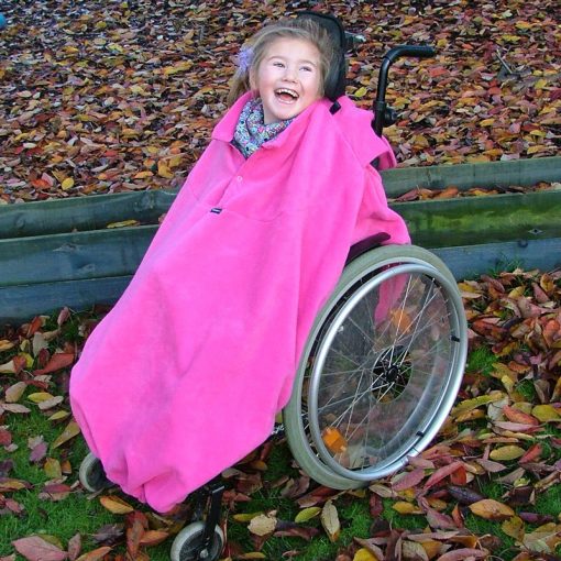 Image shows a photograph of a young girl in an outdoor, autumnal setting, laughing whilst sat in a wheelchair wearing a fuchsia total cover fleece