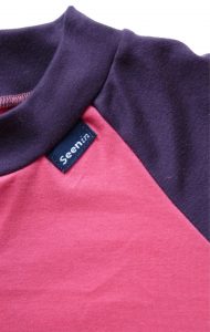 Image shows a photograph of a close-up of the collar and chest area of a Seenin sleepsuit in pink and purple