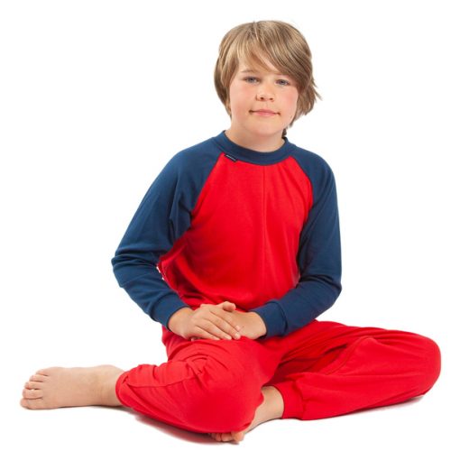 Image shows a photograph of a young boy sitting on the floor with knees bent to the side, hands on his lap, wearing a red and navy blue sleepsuit