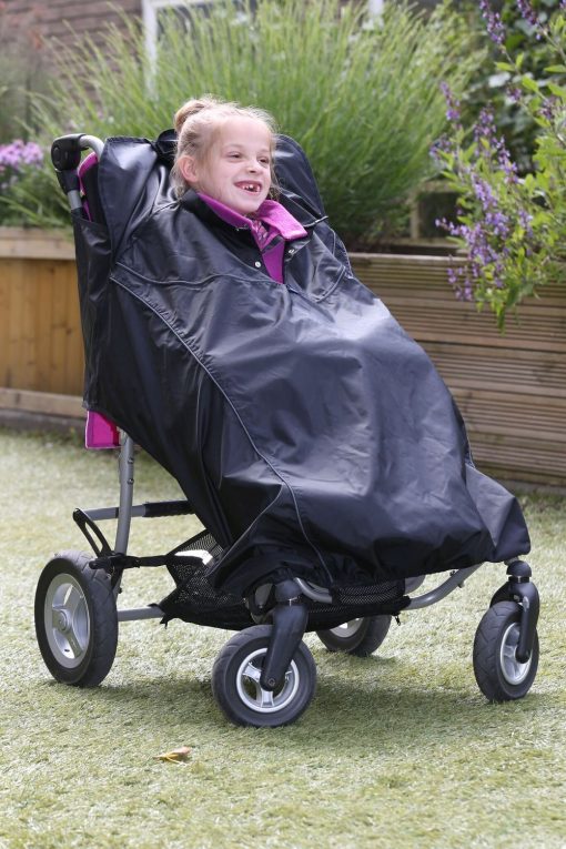 Image is a photograph of a smiling girl outdoors, sat in an adaptive SEN stroller, wearing a Seenin total wheelchair protector