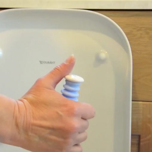 Image is a photograph of a home bathroom with someone holding their thumb over the end of the Easywipe to detail where the tissue release button is located