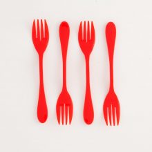 Image is a photograph of 4 red, plastic Knorks top-to-tail in a line, lay flat on a white background