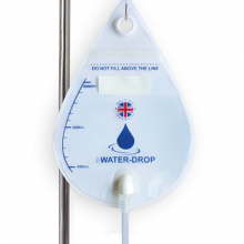 Image is a photograph of a tear-drop shaped fluids bag hanging from an IV stand