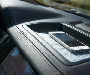 Image is a photograph of a mobile phone sat atop a strip of Cat Tongue Grip Tapeh which has been secured to a car dashboard