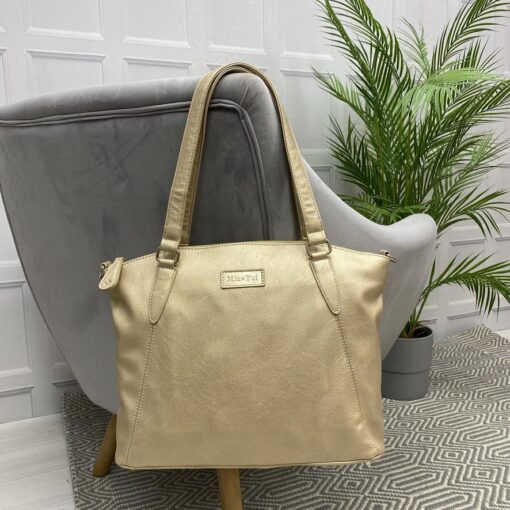 Image is a photograph of a Gold Samantha Renke accessible handbag in the extra size, hanging by the straps over the back of a grey velvet chair in a living room.