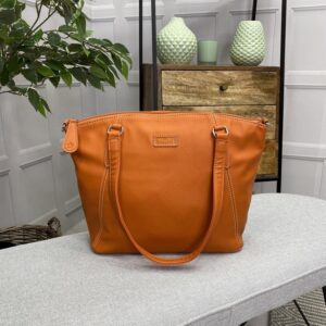 Image is a photograph of the Samantha Renke accessible handbag in Burnt Orange on a white table in a modern living room