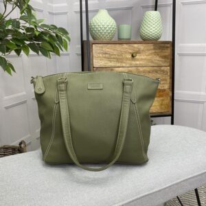 Image is a photograph of the Samantha Renke accessible handbag in Olive on a white table in a modern living room